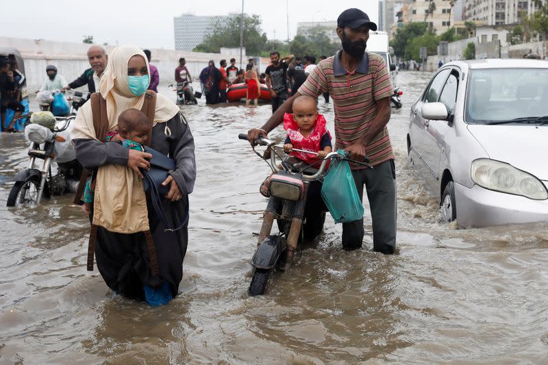 A family wades through a flooded road during the monsoon season, in Karachi