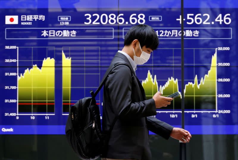FILE PHOTO: A man walks past an electric monitor displaying Japan's Nikkei share average and recent movements, outside a bank in Tokyo