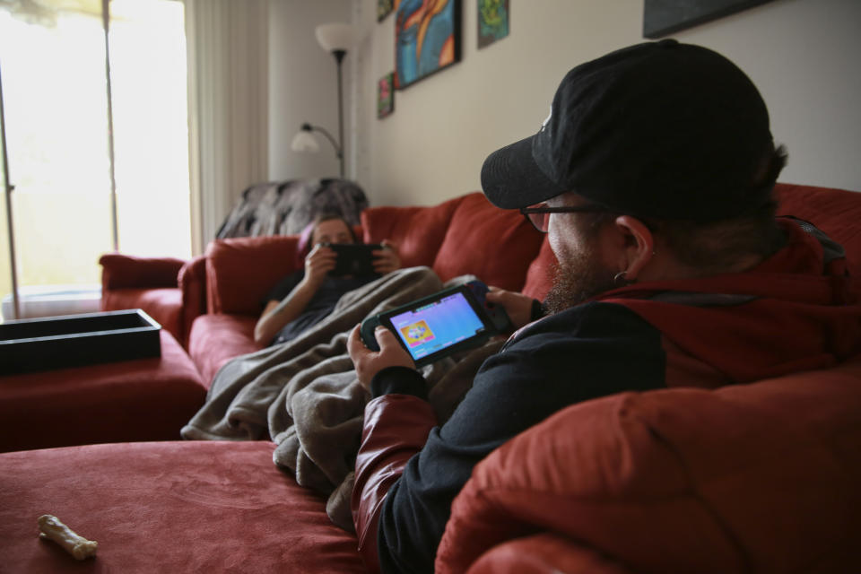 Lucas, left, and Eli play video games on their couch at their home in Casselberry, Fla., May 29, 2023. The Associated Press is not using Eli’s and Lucas’ last names because they fear reprisal. After recent legislation caused Lucas to lose access to his gender affirming care, the couple began making plans to leave Florida, a decision they aren't making lightly. (AP Photo/Laura Bargfeld)