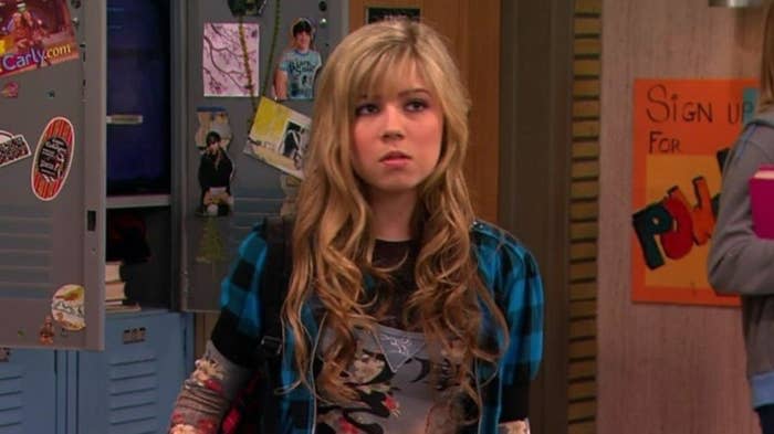 Character Sam from the show "iCarly" stands in front of lockers, wearing a layered shirt and expressing surprise