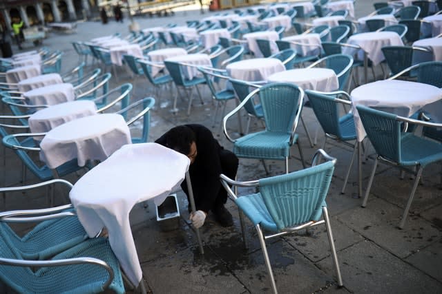 A waiter cleans tables and chairs in an empty restaurant terrace at St Mark’s Square in Venice