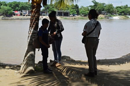 Agent of the National Migration Institute checks the IDs of people who have crossed the Suchiate River on a raft from Tecun Uman, Guatemala, to Ciudad Hidalgo, as seen from Ciudad Hidalgo