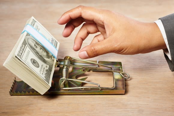 A person reaching for a stack of cash being used as bait in a mouse trap.