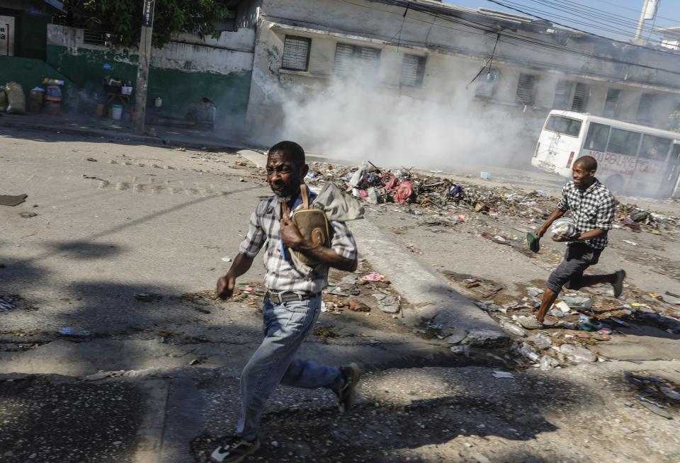 Men run for cover as riot police launch tear gas in an effort to disperse people near the National Palace, in Port-au-Prince, Haiti, Tuesday, April 2, 2024. (AP Photo/Odelyn Joseph)