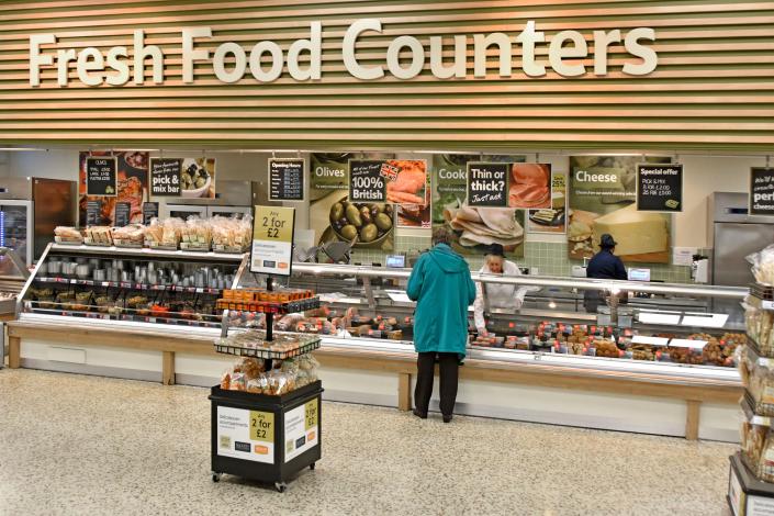 Tesco Extra supermarket store interior Fresh Food Counter back view woman shopper customer being served meat products early morning London England UK