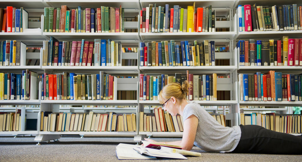 A university student studies while lying on a library floor.