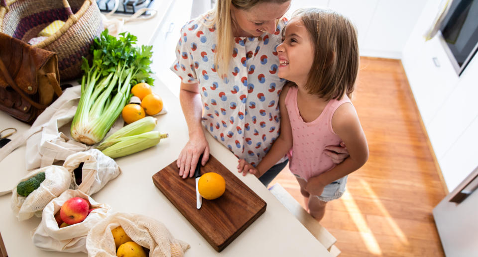 Woman and daughter get ready to chop orange in the kitchen.