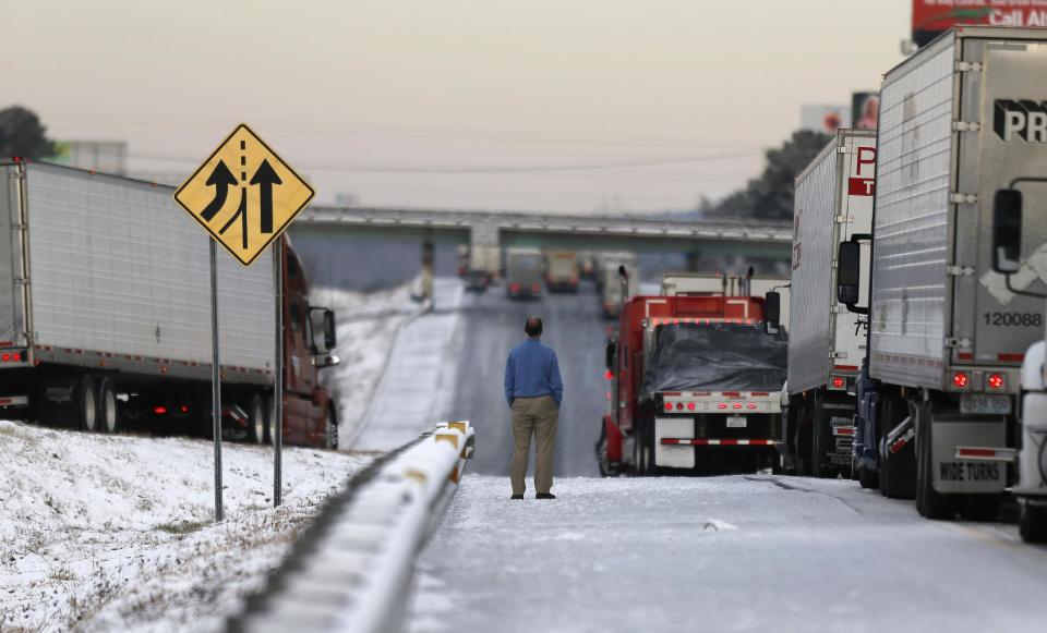 A man stands on the frozen roadway as he waits for traffic to clear along Interstate 75 Wednesday, Jan. 29, 2014, in Macon, Ga. A winter storm dumped snow and covered parts of the state with ice. Gov. Nathan Deal said early Wednesday that the National Guard was sending military Humvees onto Atlanta's snarled freeway system in an attempt to move stranded school buses and get food and water to people. (AP Photo/John Bazemore)