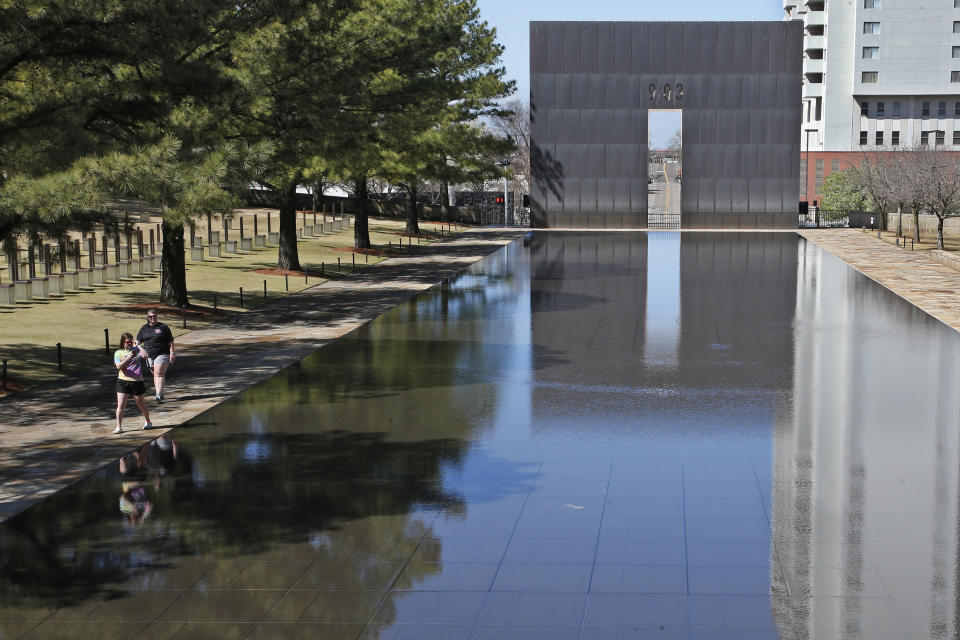 FILE - In this March 18, 2020 file photo, visitors walk next to the reflecting pool at the Oklahoma City National Memorial and Museum in Oklahoma City. The Oklahoma City National Memorial and Museum has announced that it will offer a recorded, one-hour television program in place of a live ceremony to mark the 25th anniversary of the Oklahoma City bombing due to concerns about the spread of the coronavirus. (AP Photo/Sue Ogrocki, File)