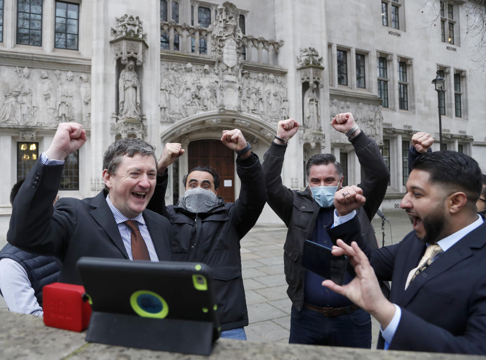 Uber drivers of the (ADCU), App Drivers & Couriers Union, celebrate as they listen to the court decision on a tablet computer outside the Supreme Court in London, Friday, Feb. 19, 2021. The U.K. Supreme Court ruled Friday that Uber drivers should be classed as “workers” and not self employed.(AP Photo/Frank Augstein)