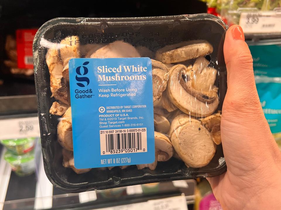 hand holding up a container of sliced white mushrooms at target