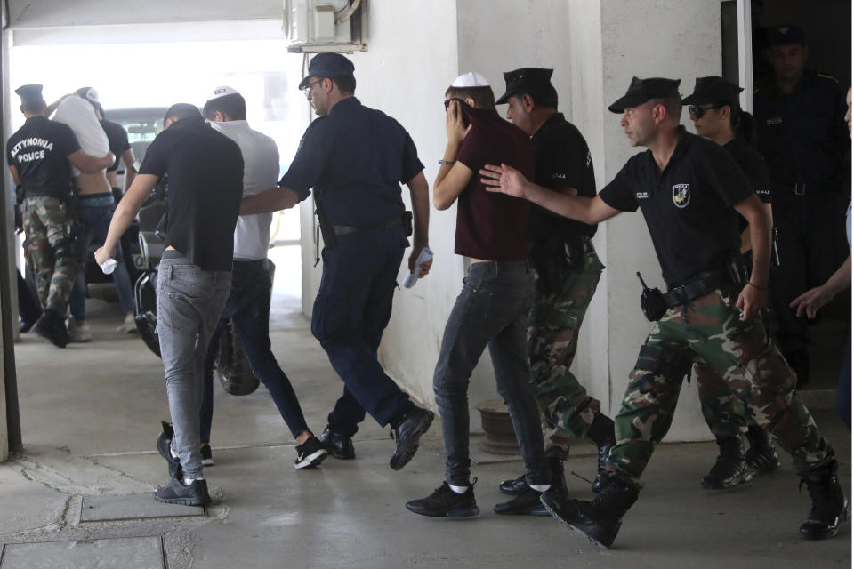 Suspects cover their faces with their shirts as they arrive at the Famagusta courthouse in Paralamni, Cyprus, Friday, July 26, 2019. A Cyprus court has extended the detention of seven Israeli teenagers out of the 12 who were arrested as suspects in the rape of a 19-year-old British woman. (AP Photo/Petros Karadjias)