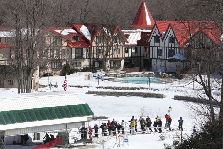 Skiers line up to board the Heather Express lift at The Highlands at Harbor Springs, with the resort's main lodge visible in the background.