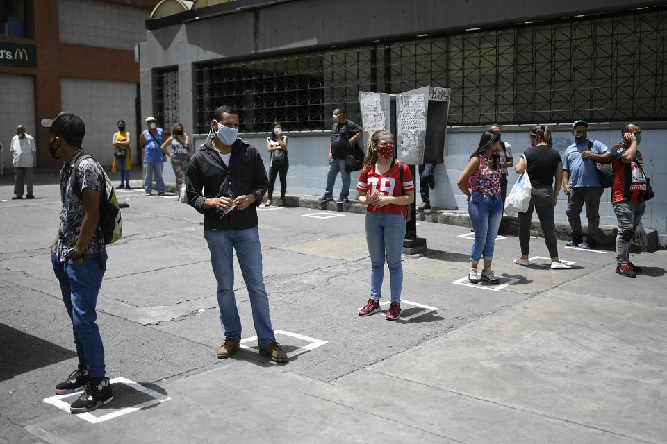 Commuters stand on visual cues to encourage social distancing, as a precaution amid the spread of the new coronavirus, at a bus stop in downtown Caracas, Venezuela, Monday, June 29, 2020. (AP Photo/Matias Delacroix)