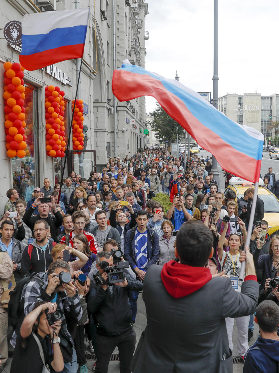 Russian opposition candidate and activist Ilya Yashin, back to a camera, waves a Russian flag during a protest in Moscow, Russia, Sunday, July 14, 2019. Opposition candidates who run for seats in the city legislature in September's elections have complained that authorities try to bar them from the race by questioning the validity of signatures of city residents they must collect in order to qualify for the race. (AP Photo/Pavel Golovkin)