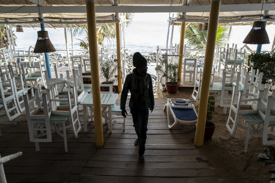 In this Thursday, March 26, 2020, photo, a security guard walks in a normally busy but now closed restaurant on a beach in Dakar, Senegal. As African countries have started shutting down borders and economic activity plummets, those who do informal work or run small businesses are suffering without the type of economic assistance that some countries in the developed world are able to provide. (AP Photo/Sylvain Cherkaoui)