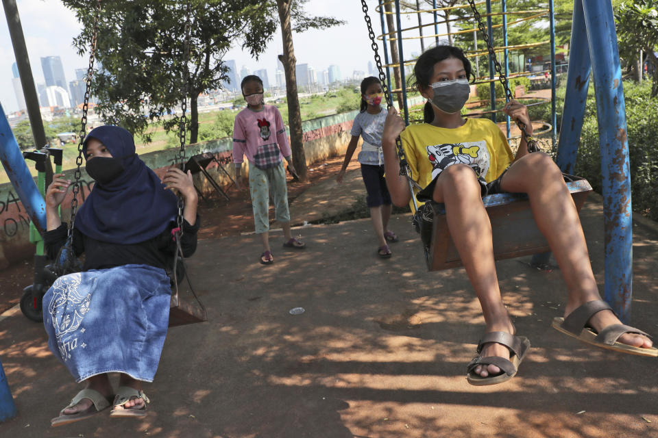 Indonesian children wearing face masks as a precaution against coronavirus outbreak play on swings in Jakarta, Indonesia, Wednesday, Sept. 23, 2020. (AP Photo/Tatan Syuflana)