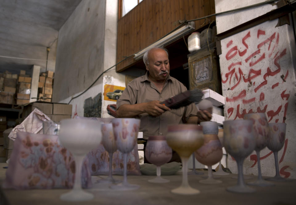 In this Saturday, July 6, 2019 photo, Abed Abu Sedou, removes the dust from samples of hand-painted glasses are displayed on a table in his closed glass factory in Gaza City. Talk about old Gaza, and what pops up are images of clay pottery, colorful glassware, bamboo furniture and ancient frame looms weaving bright rugs and mats. As such professions could be dying worldwide, the pace of their declining is too fast in Gaza that out of its some 500 looms, only one is still functioning. (AP Photo/Khalil Hamra)