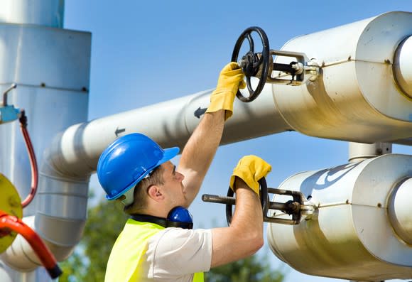 A man wearing a hard hat turning valves on a natural gas pipeline