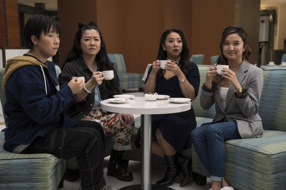 Four people holding white coffee cups look at something offscreen. They are sitting at a table on green couches. (Ed Araquel / Lionsgate)