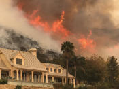 FILE - In this Thursday, Dec. 14, 2017, file photo provided by the Santa Barbara County Fire Department, shows flames from a back firing operation underway rise behind a home off Ladera Ln near Bella Vista Drive in Santa Barbara, Calif. A Southern California utility has agreed to pay $360 million to settle lawsuits brought by cities, counties and other public agencies over deadly wildfires sparked by its equipment in the last two years, including one that was later blamed for a mudslide that killed more than 20 people. An attorney for 23 public entities said Wednesday, Nov. 13, 2019, that Southern California Edison has agreed to the sum to repay taxpayers for firefighting and damage from the Thomas Fire in 2017 and Woolsey Fire last year. (Mike Eliason/Santa Barbara County Fire Department via AP,File)