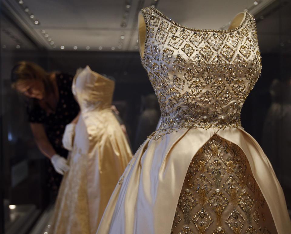 In this photo taken Monday, July 1, 2013, an employee fixes a dress of Queen Elizabeth II on display at the Fashion Rules exhibition at Kensington Palace in London. Opening on 4 July, a new glamorous exhibit at Kensington Palace showcases how the styles of three royal ladies; Queen Elizabeth II, her sometimes risque sister Margaret, and the glamorous Princess Diana, each reflected and influenced the trends of their fashion heyday. (AP Photo/Frank Augstein)