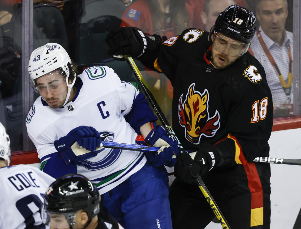 Vancouver Canucks defenseman Quinn Hughes, left, is checked by Calgary Flames forward A.J. Greer, right, during third-period NHL hockey game action in Calgary, Alberta, Thursday, Nov. 16, 2023. (Jeff McIntosh/The Canadian Press via AP)