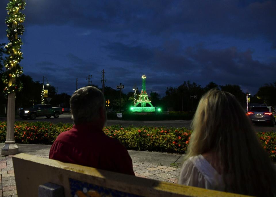 Jim (left) and Susanne LoPilato sit on a bench as traffic drives by the 12.5-foot Eiffel Tower replica at the roundabout at Dixie Highway and Martin Avenue near their home, Thursday, Dec. 8, 2022, in Rio. It took Jim roughly 80 hours to build the tower. "He doesn't want to go to Paris so he brought Paris to me," said Susanne. The family also decorated 25 street lights heading in all directions from the roundabout, making them look like giant candy canes.