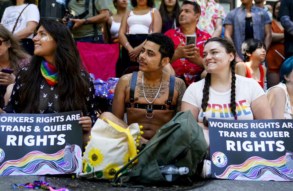 FILE - Jessica Garcia, Erik Garcia and Meara White hold signs in support of Starbucks workers as they watch marchers in the annual Seattle Pride Parade, Sunday, June 25, 2023, in Seattle. The union organizing Starbucks workers said Monday, June 26, 2023, that a strike timed to Pride month closed 21 stores over the weekend, including the company’s flagship Reserve Roastery in Seattle. The strike will continue through this week and is expected to close or disrupt operations at more than 150 stores, Starbucks Workers United said. (AP Photo/Lindsey Wasson, File)