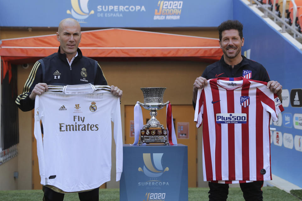 El francés Zinedine Zidane (izquierda), técnico del Real Madrid, y el argentino Diego Simeone, estratega del Atlético de Madrid, posan con las camisetas de sus equipos, flanqueando el trofeo de la Supercopa en Yeda, Arabia Saudí, el sábado 11 de enero de 2020 (AP Foto/Hassan Ammar)