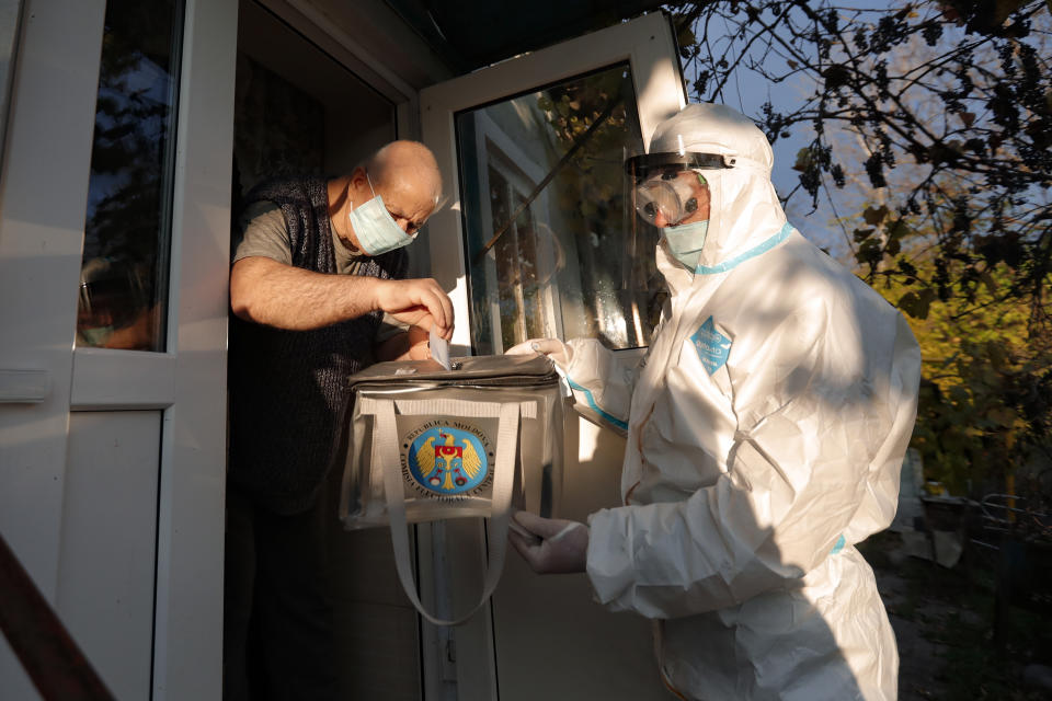 An election official wearing a biohazard suit, for protection against the COVID-19 infection, holds a mobile ballot box as a man casts his vote in the presidential elections in Hrusova, Moldova, Sunday, Nov. 15, 2020. Moldovans returned to the polls Sunday for the second round of voting in the country's presidential election, facing a choice between the staunchly pro-Russian incumbent and his popular pro-Western challenger after former prime minister, Maia Sandu, who beat the odds to win the first round on November 1 with over 36 percent of to vote, leaving the incumbent, President Igor Dodon, trailing her by over 3.5 points. (AP Photo/Roveliu Buga)