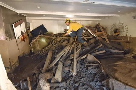 Santa Barbara County Firefighter Vince Agapito searches through a home destroyed by mudflow and debris in Montecito, California, U.S., January 13, 2018. Mike Eliason/Santa Barbara County Fire/Handout via REUTERS