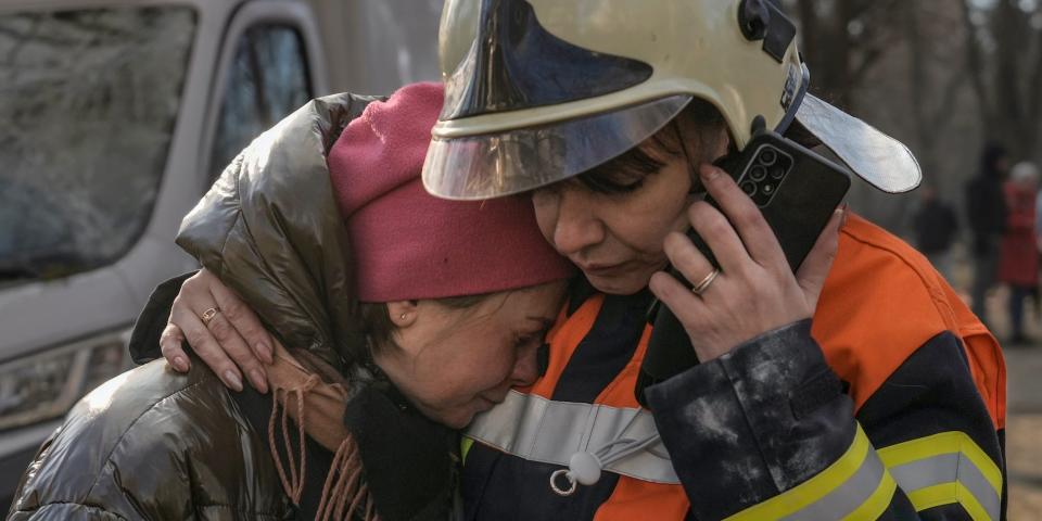 A firefighter comforts a woman outside a destroyed apartment building after a bombing in a residential area in Kyiv, Ukraine, Tuesday, March 15, 2022.