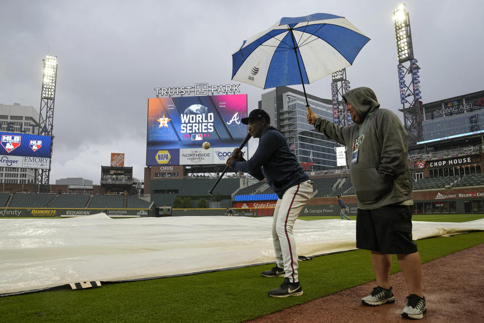 A crew member holds an umbrella for Atlanta Braves third base coach Ron Washington as he hits balls during batting practice before Game 3 of baseball's World Series between the Houston Astros and the Atlanta Braves Friday, Oct. 29, 2021, in Atlanta. (AP Photo/Ashley Landis)