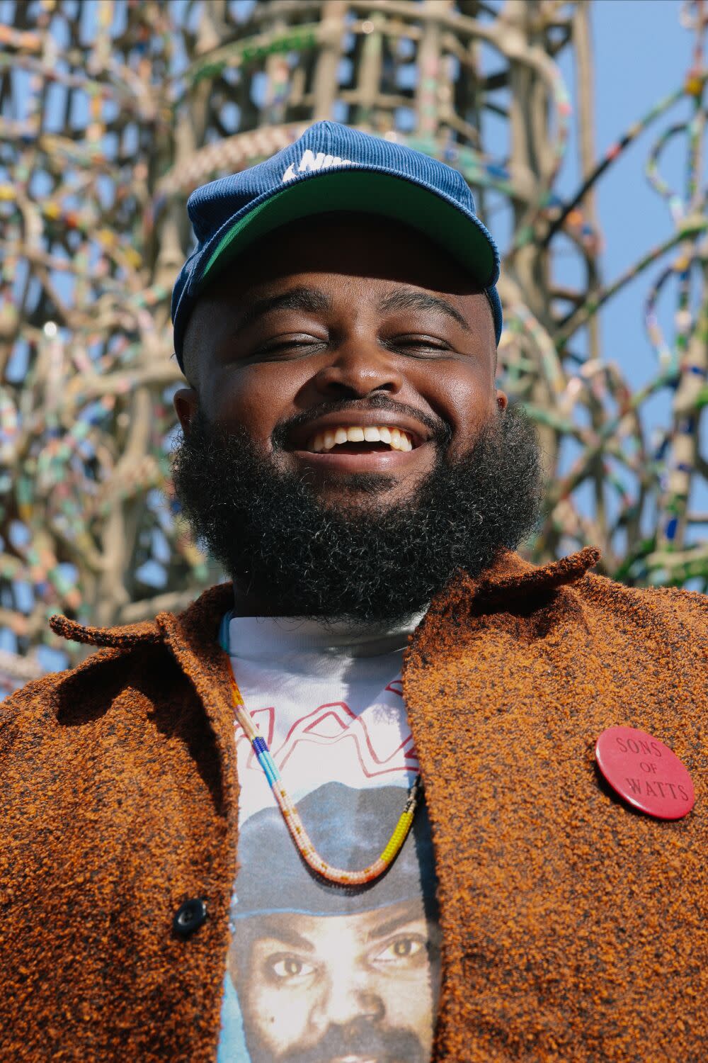 A man stands in front of the Watts Towers smiling.