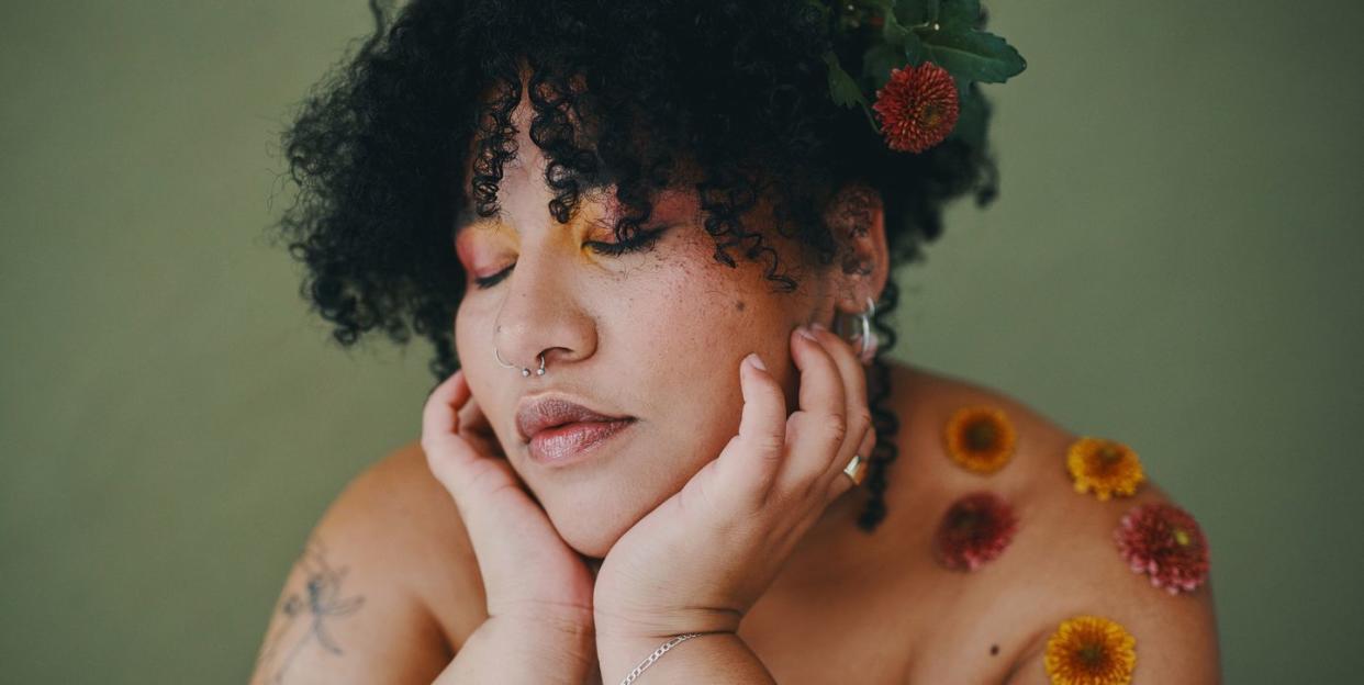 shot of a beautiful young woman covered in petals against a green studio background