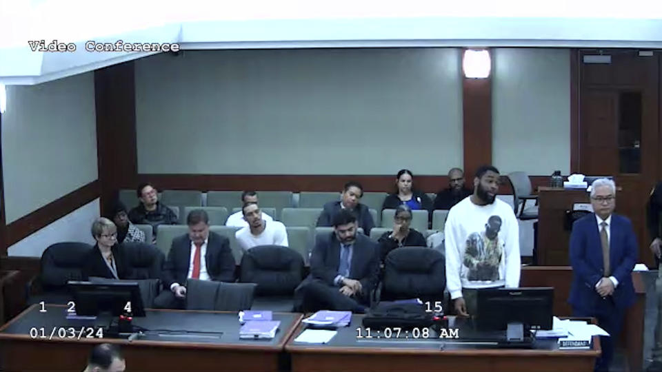 In this image from video provided by the Clark County District Court, defendant Deobra Redden in a white long-sleeved shirt is seen standing next to his defense attorney at his sentencing in a felony battery case, Wednesday, Jan. 3, 2024 in Las Vegas. The image shows the defendant before he launched over Clark County District Court Judge Mary Kay Holthus' desk, starting a fight with courtroom officers and staff, according to the video and court officials. (Clark County District Court via AP)