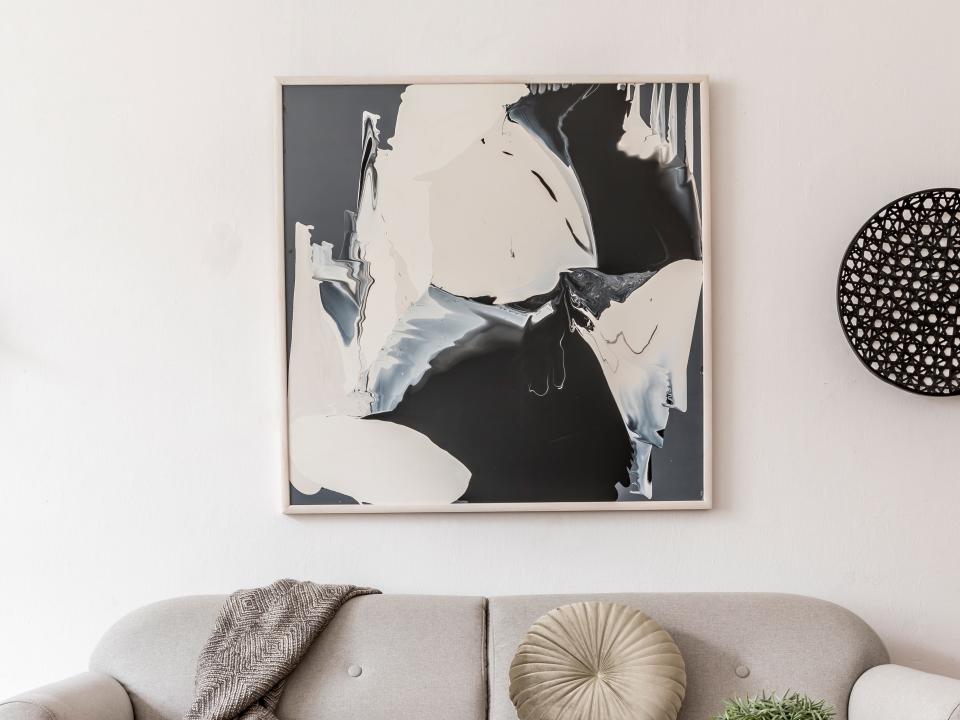 Black and white abstract art on wall with black circular decoration to the right of it and gray couch below