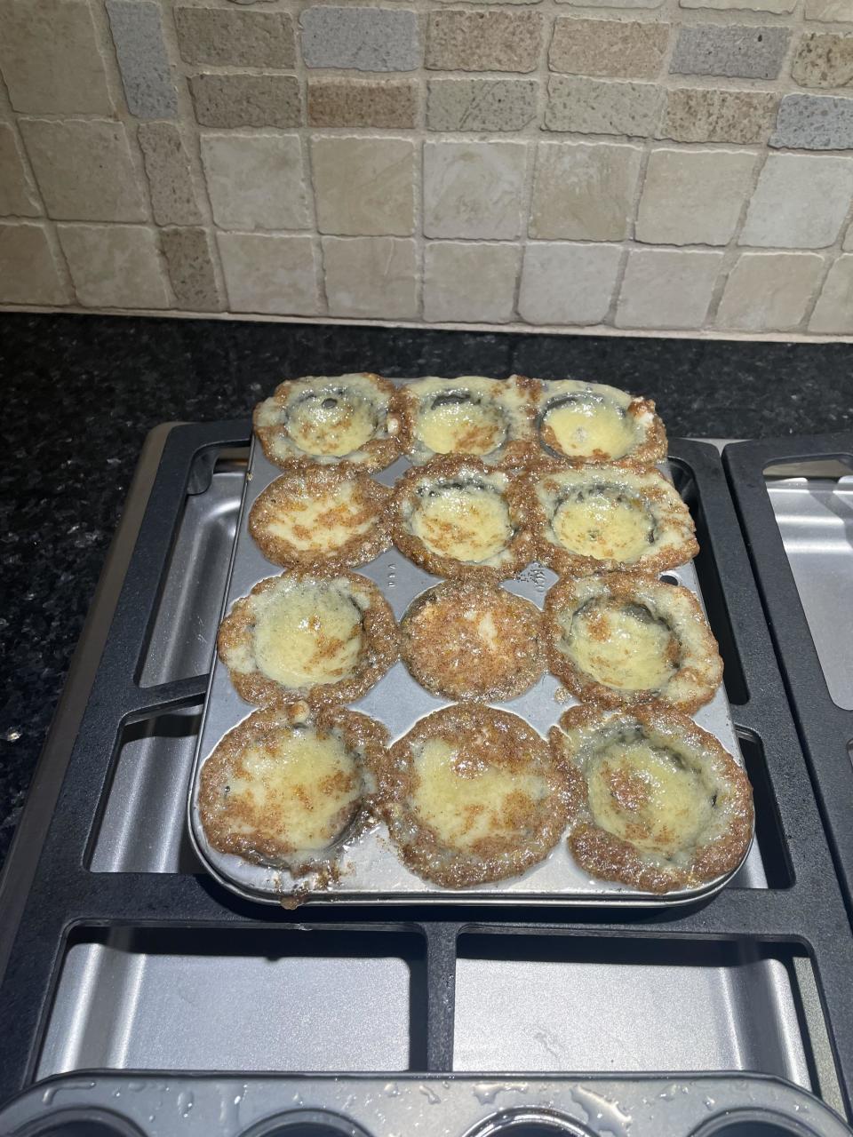 A tray of freshly baked  muffins on a stovetop that are raw and have caved in the center