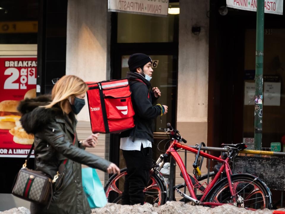 A DoorDash rider with his bike and delivery pack on his back exiting a NYC restaurant in winter.