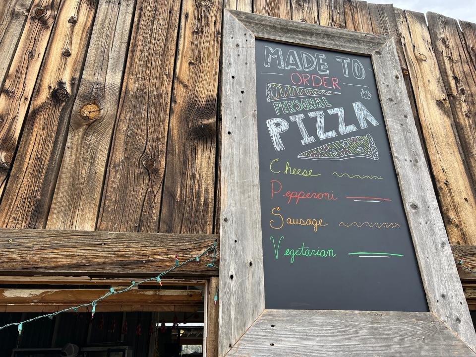 A chalkboard sign next to wood paneling that says made to order pizza with options below it