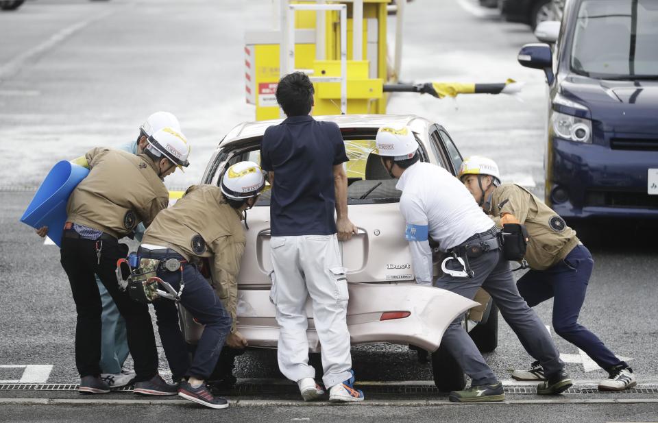 People move a car which was flown by strong wind caused by a powerful typhoon in Osaka, western Japan, Tuesday, Sept. 4, 2018. A powerful typhoon blew through western Japan on Tuesday, causing heavy rain to flood the region's main offshore international airport and high winds to blow a tanker into a connecting bridge, disrupting land and air travel. (Kota Endo/Kyodo News via AP)