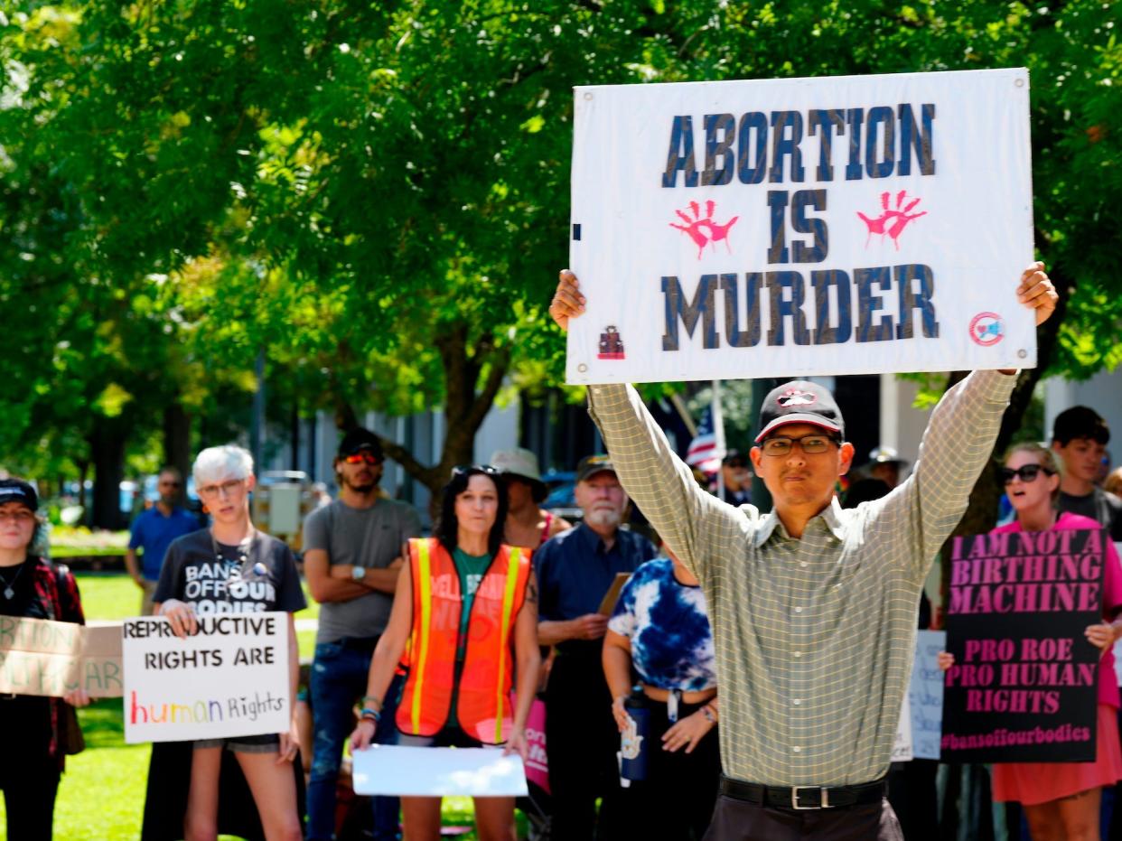 A man supporting restrictions on abortion holds a sign as abortion-rights supporters hold signs behind him outside the South Carolina Statehouse on Thursday, July 7, 2022, in Columbia, S.C.