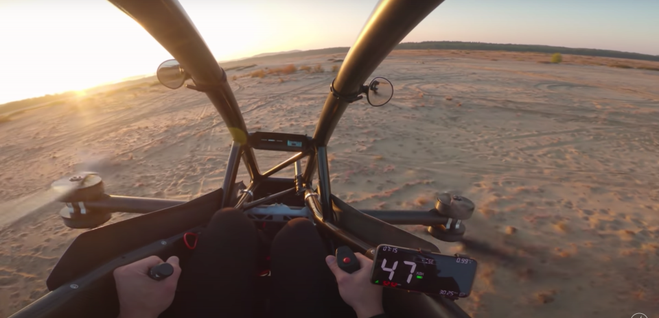 A Jetson One all-electric personal aircraft hovering over a sandy beach at sunset.