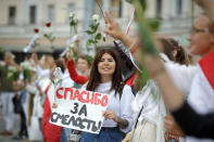 Belarusian opposition supporters hold flowers and flash victory signs during a protest in Victory Square in Minsk, Belarus, Thursday, Aug. 20, 2020. Demonstrators are taking to the streets of the Belarusian capital and other cities, keeping up their push for the resignation of the nation's authoritarian leader. President Alexander Lukashenko has extended his 26-year rule in a vote the opposition saw as rigged. Banner reads "Thank you fot the Bravery". (AP Photo/Sergei Grits)