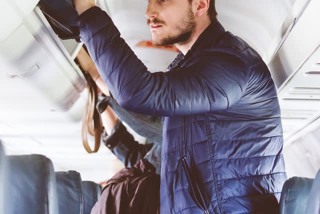 <p>izusek/Getty</p> Passenger getting their luggage from the overhead bin