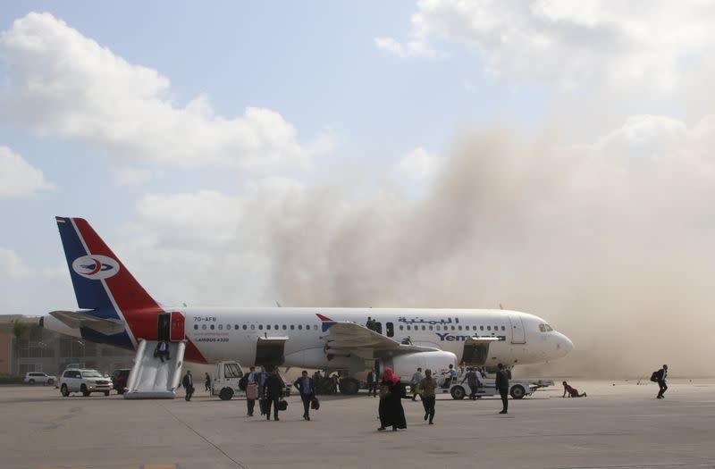 Gente camina sobre la pista mientras el polvo y el humo se elevan después de que explosiones golpearan el aeropuerto de Aden, a la llegada del gobierno yemení recién formado a Aden, Yemen. 30 de diciembre de 2020.