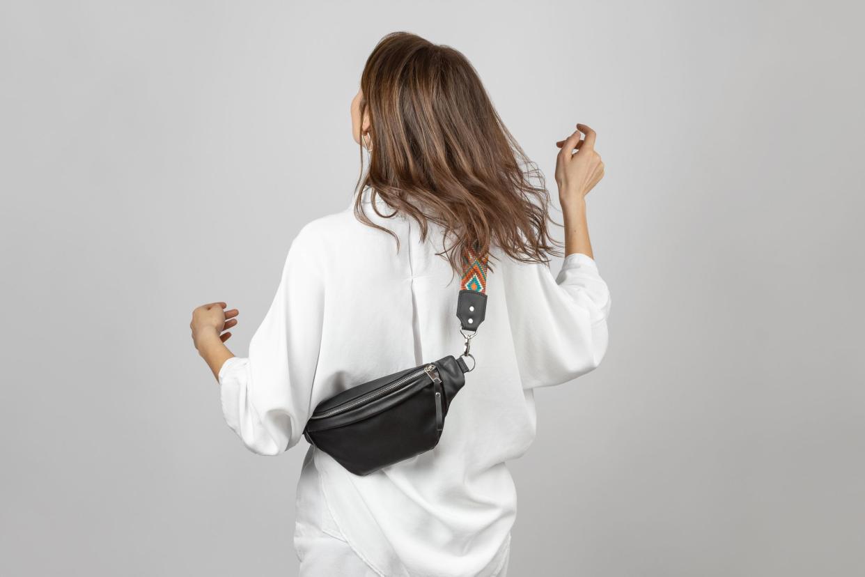 White Woman Wearing White Jeans, Shirt and Crossbody Black Leather Belt Bag over Grey Background