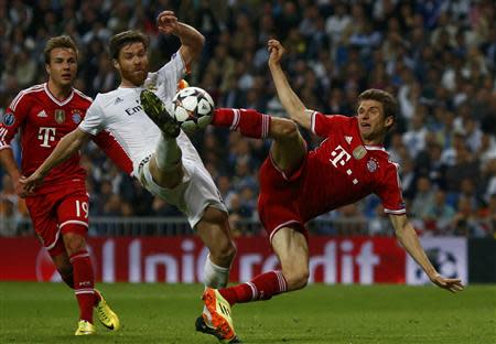 Real Madrid's Xabi Alonso kicks the ball in front of Bayern Munich's Mario Goetze (L) and Thomas Mueller (R) during their Champion's League semi-final first leg soccer match at Santiago Bernabeu stadium in Madrid, April 23, 2014. REUTERS/Michael Dalder