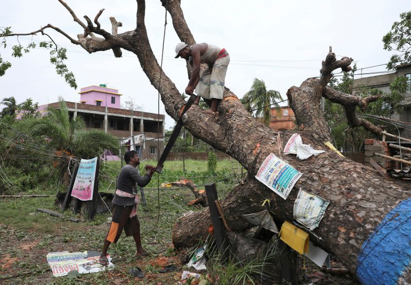 Men cut branches of an uprooted tree in the aftermath of Cyclone Amphan, in South 24 Parganas